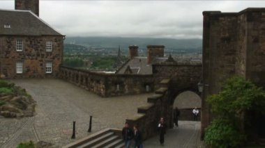 İskoçya'nın Edinburgh kalesinde bir kemerin altında taş bir yol yürürken insanlar.
