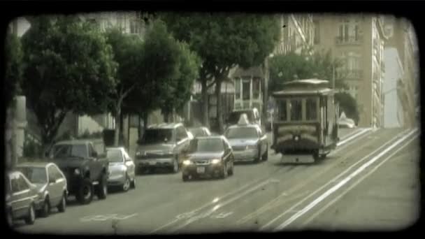 伝統的なトロリー車来る車 緑の木々 そして高層ビルが並ぶサンフランシスコ通りに車の横にある丘の上通りのトラックを転がり落ちる ビンテージの様式化されたビデオ クリップ — ストック動画