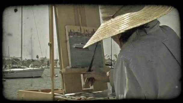中景的女艺人 穿着一件蓝色的衬衫和太阳帽 她仔细地描绘大海的格式副本以及从边缘封闭锚的船停靠在加利福尼亚州纽波特海滩附近 — 图库视频影像