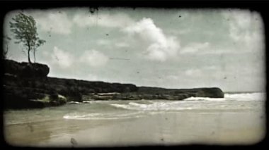 Dalgalar Hawaii plajda, kayalık Lavataş çıkıntıya bir ağaç bulutlar ile noktalı mavi gökyüzü altında üst yanındaki kumlu dağ geçidi alanına giriyor. Vintage stilize video klip.