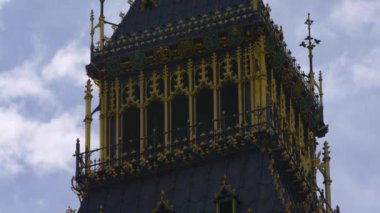 Londra'daki Big Ben saat kulesinin üst kısmının yakın çekim. Kamera kulede yavaşça aşağı doğru hareket eder. Saat kısmı görülmez. Mavi gökyüzü ve bulutlarla çevrili.