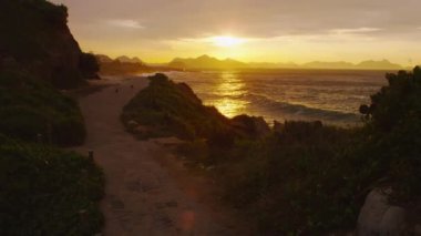 Rio de Janeiro Ipanema plaj üzerinde gün batımı ile arka planda kir yol izleme çekim. Güneş, suyun üzerindeki bulutların arasından parlar..