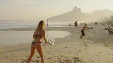 Rio De Janeiro, Brezilya - Haziran 2013: Ters açı yavaş hareket, topa vurmak için çerçeve dışında tökezledi bir adam ile Ipanema plajda tenis oynayan bir kız dolly dışarı görüntüleri