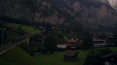 Şafakta İsviçre Lauterbrunnen'in soldan sağa şutunu çekti. Bir tren sol tarafta sürünen görülebilir. Şehir ve tarihi şehir kiliseye doğru kayalık kayalıklar üzerinde güneş ışığı ışınları.