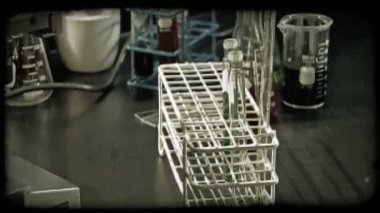 Erkek raf kamera tava üzerinde ve laboratuar mikroskobu kadar süre sıralama içine renkli sıvı ile dolu kadehler koyar. Vintage stilize video klip.