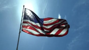 Amerikan bayrağı dalgalardan bir bayrak direğine arkadan aydınlatmalı kör edici bir güneş mavi gökyüzü altında tarafından