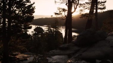 Ağaçların arasından görülebilen güneşin karanlık görüntüsü. Akarsu ve nehir görünür. Emerald Bay State Park, Lake Tahoe, Kaliforniya'da vuruldu.
