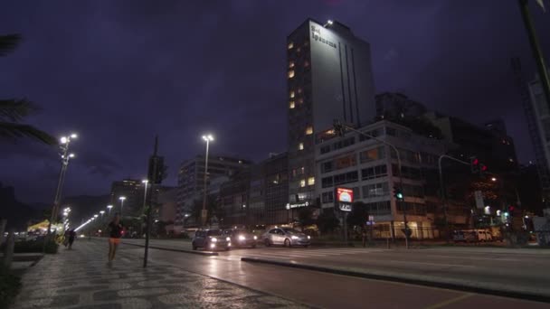ジャネイロ ブラジル 2013 オレンジ色のパンツとランナーとコパカバーナ歩道パターンのショットをパンします トラフィックは 中央値で区切られます 高層ビルやヤシの木々 が表示されます 夜の撮影 — ストック動画