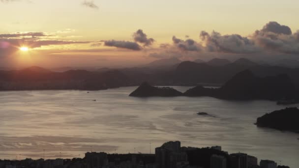 ショット 日没時にリオデジャネイロの街の 右からカメラのパンをゆっくりと残しました 街と湾をフレームの下に見ることが 山が遠くにシルエット — ストック動画