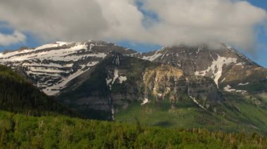 Karla kaplı dağ silsilesi, çam ağaçlarının altında ön planda uzun bulunduðu hızlandırılmış bulut örtüsü döner altında arka planda, görkemli.