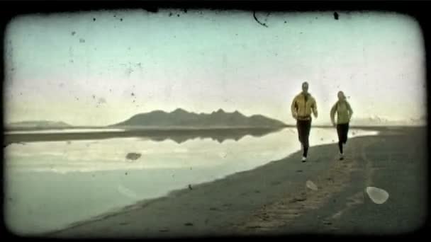 男人和女人 身穿健身服和携带齿轮 慢跑稳步朝着摄像机沿 Soflty 点燃海滩 Alonside 游泳池的水 反映洛矶山脉和晨雾 — 图库视频影像