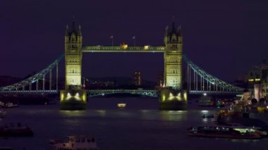 Akşam aydınlatılmış Tower Bridge (Londra) sabit çekim. Arabalar köprüden geçiyor ve Thames Nehri'nde tekneler var..