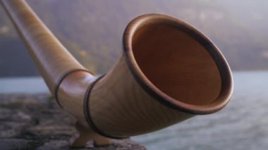Bir alphorn'un açık ağzının raf-odak yakın çekim ilerler gibi bir gölün kenarında ki taş duvara dayanıyor. Mountians arka planda, gölün diğer tarafında yükselir. Filme din İsviçre.