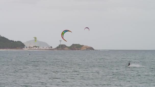 平移镜头离岸开放海洋和滑翔伞的冲浪者 不同可见滑翔伞冲浪者 科帕卡巴纳城市景观泛年底是可见的 山是城市以外的景象 天空是朦朦胧胧 — 图库视频影像