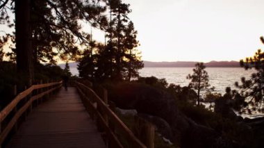 Yolda yürüyen bir adamın statik görüntüsü. Adam kameraya yaklaşırken bir geçitte çekilen çekim. Sand Harbor State Park, Lake Tahoe, Nevada bakan Kum Limanı etrafında boardwalk gün batımında filme.