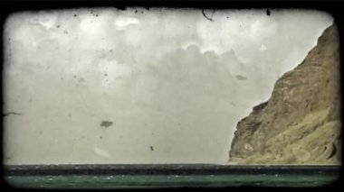 Derin mavi ve yeşil suları ve dalgalar kıyıya doğru kayalık uçurum su arka planda ve dramatik bulutlar gökyüzünde yükselen ile geliyor. Vintage stilize video klip.