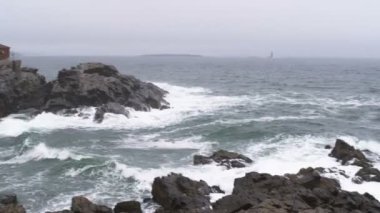 Çekim dalgaları üzerinde kayalık bir kıyı breaking Portland Head ışık ve onun dönen beacon için kaydırma. Cape Elizabeth, Maine.