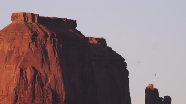 赤い岩崖との距離で動力パラグライダーの静的なショット 太陽の光が赤い岩の つの側面で目に見える — ストック動画