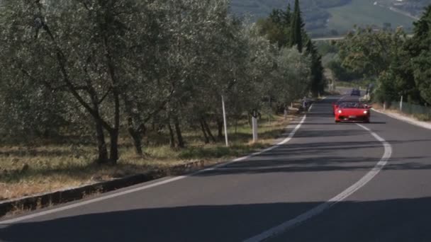 Široký záběr na dvě Ferrari, jízdy na venkovské silnici