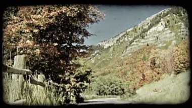 Hala sonbahar ağaçları, ahşap çit ve arka planda mavi gökyüzü yanında uzun dağ zirvesi ile çevrili çakıl yol eğimli dağ vurdu. Vintage stilize video klip.