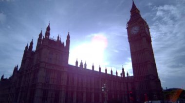 Londra'da Big Ben saat kulesinin sabit çekim, öğleden sonra çekildi. Güneş ışığı göz kamaştırıcı ve gökyüzünde bazı bulutlar var. Sahnenin köşelerinde, çevredeki insanların bazı ilginç yansımaları görülebilir.