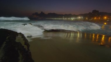 Yavaş çekim, kum ve sörfçü karşı çökmesini dalgaların sağ pan arka planda şehrin parıltısı ile geceleri Ipanema plajda gelgit atılan