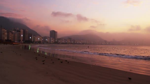 在里约热内卢 巴西采取在日落海滩附近冲浪桨板冲浪者的远距离拍摄 看见一个人在海滩上慢跑 — 图库视频影像