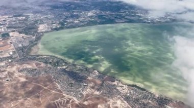View from airplane looking down Saratoga Springs and Utah Lake while flying past clouds.
