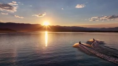 Two people riding personal watercraft's into the sunset at Hebgen Lake in Montana.