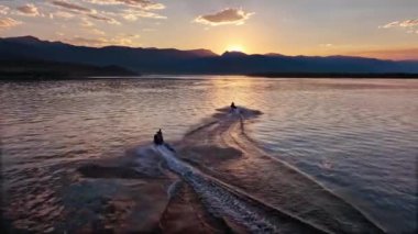 Following people riding on personal watercraft's from aerial view during sunset on Hebgen Lake in Montana.