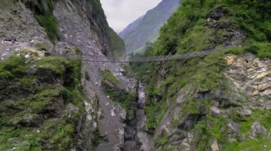 Person hiking over bridge spanning deep canyon in Nepal flying past looking at river in the gorge below.