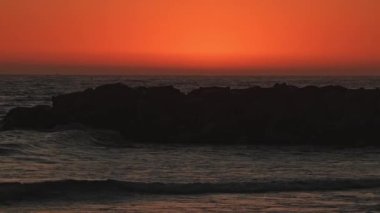 Kaliforniya kıyılarında gökyüzü turuncu ışıldarken yavaş çekimde dalgalar sallanıyor..
