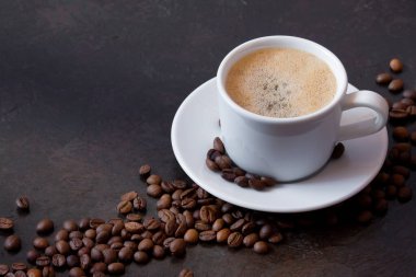 Kahve fincanının üzerinde koyu kahve çekirdekleri olan bir fincan beyaz kahve.