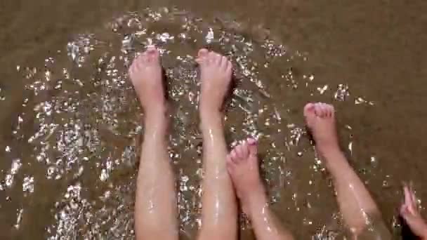 Close-up zicht op de voetjes van de meisjes die op het zandstrand liggen. Hun benen in zee golven. — Stockvideo