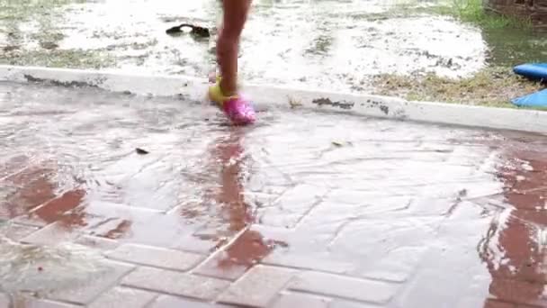 A little girl in a red swimsuit jumps after a downpour in a puddle. — Stock Video