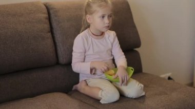 Küçük kız televizyon seyrediyor ve kanepeye oturmuş cips yiyor.