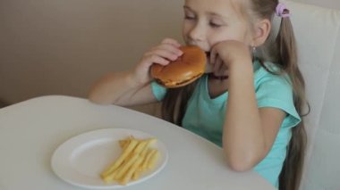 Çocukluk ve yeme konsepti. Hamburgerin ve patates kızartmasının tadını çıkaran küçük bir kız.