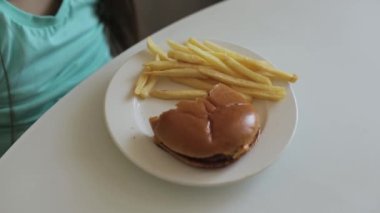 Çocukluk ve yeme konsepti. Hamburgerin ve patates kızartmasının tadını çıkaran küçük bir kız.