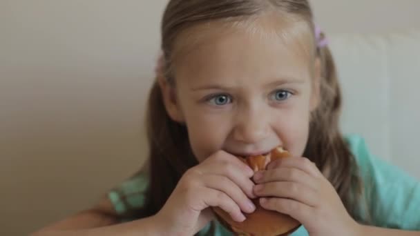 Conceito de infância e alimentação - menina desfrutando de um hambúrguer e batatas fritas na mesa desfrutando de comida insalubre — Vídeo de Stock