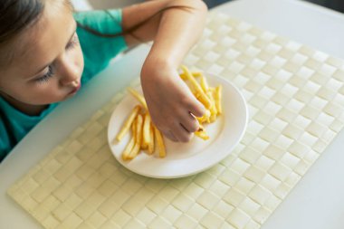 Mutfakta patates kızartması yiyen küçük bir kızın yakın çekimi.