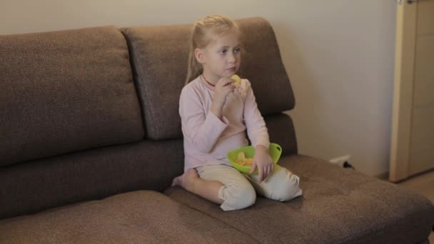Bambina guardando la TV e mangiando patatine seduti sul divano — Video Stock