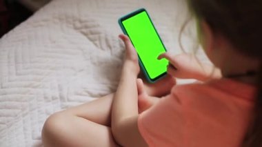 Elinde yeşil ekranlı cep telefonu olan bir kız. Kız oyun oynuyor, Mesafe Öğrenme.