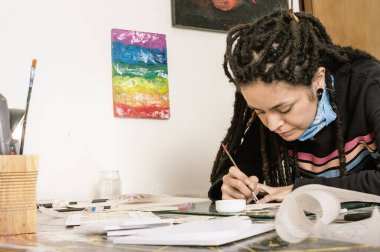 Güzel beyaz bir kız, İspanyol bir Latin sanat yönetmeni, atölyesinde çalışıyor, masasında çalışıyor, hassas kağıt ve köpük ile ince bir fırça ve beyaz yapıştırıcı yapıştırıyor..