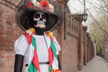 Beyaz elbiseli, siyah şapkalı, çiçekli Calavera Catrina şekerli kafatası giyen bir kadın..