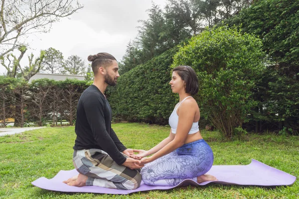 Dışarıda meditasyonda el ele tutuşan genç bir çiftin yan görüntüsü..