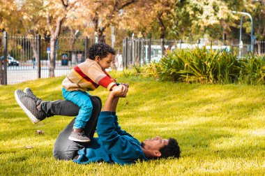 Genç baba gülümsüyor, oğluyla meydanda oynuyor.