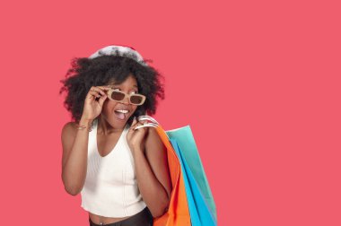 Güzel siyah Latin Amerikalı kız, afro alışverişi yapıyor, indirimler konusunda heyecandan gözlüklere bakıyor, pembe arka plan fotokopi alanından sağa, ticari konsepte geçiyor..