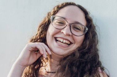 Güzel, beyaz, kıvırcık gözlüklü, kameraya bakan, duvara yaslanmış, yaşam tarzı kavramı ve gururlu Latin bir kızın portresi..