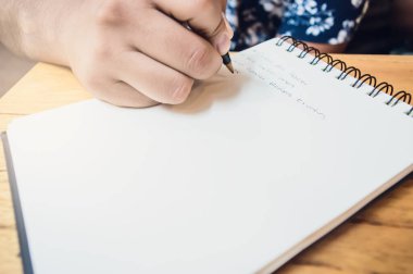 Erkek eli tükenmez kalemle ahşap bir masaya yazı yazıyor, notlar alıyor, iç kursunu yaparken yazıyor ve ders çalışıyor..