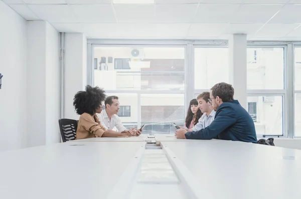 5 business people of different Hispanic Latino ethnicities, in a business office of a coworking, discussing with their phones in a business meeting.